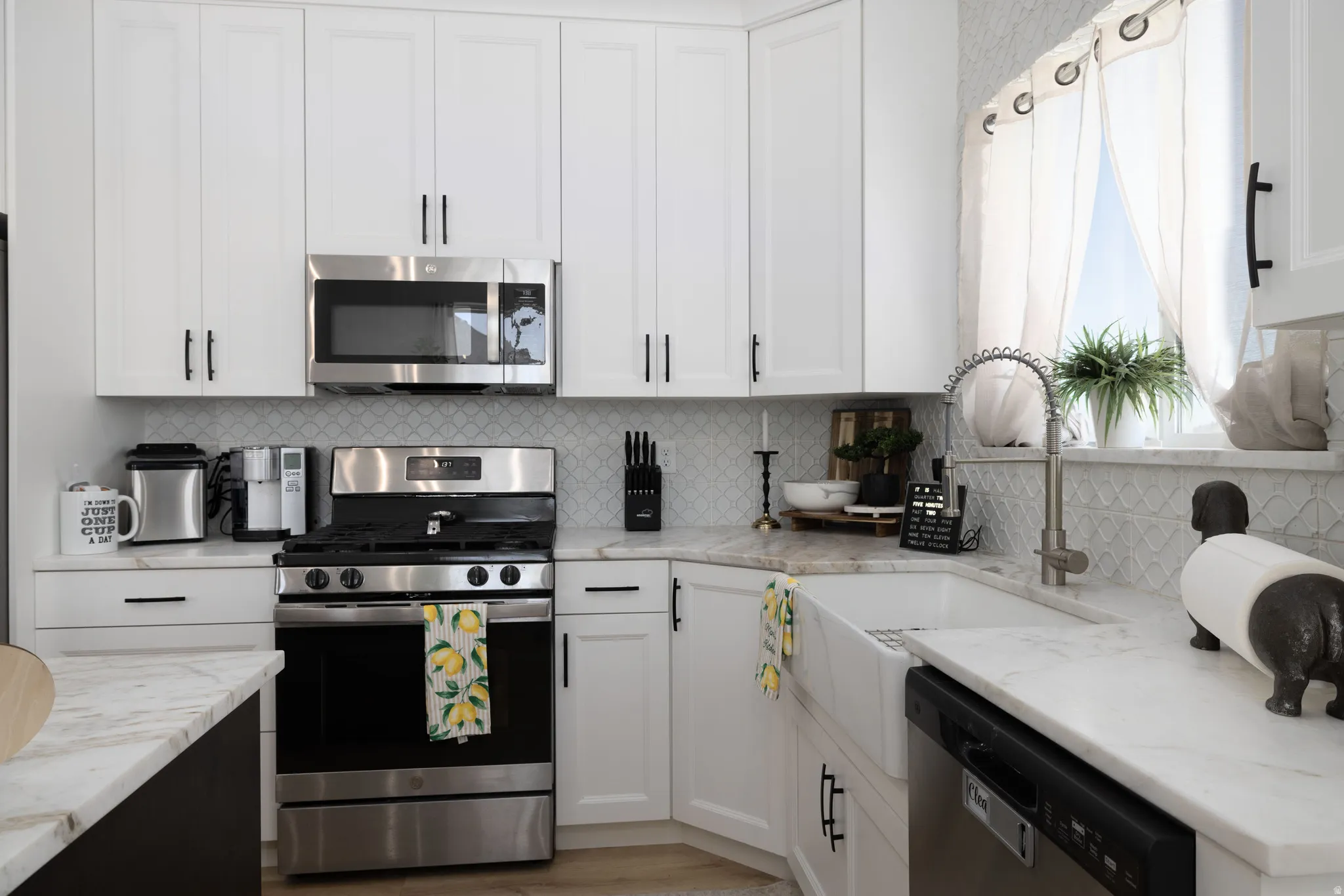 Kitchen featuring white shaker-style cabinetry, stainless steel appliances, a farmhouse sink, granite countertops, and a full-height geometric tile backsplash