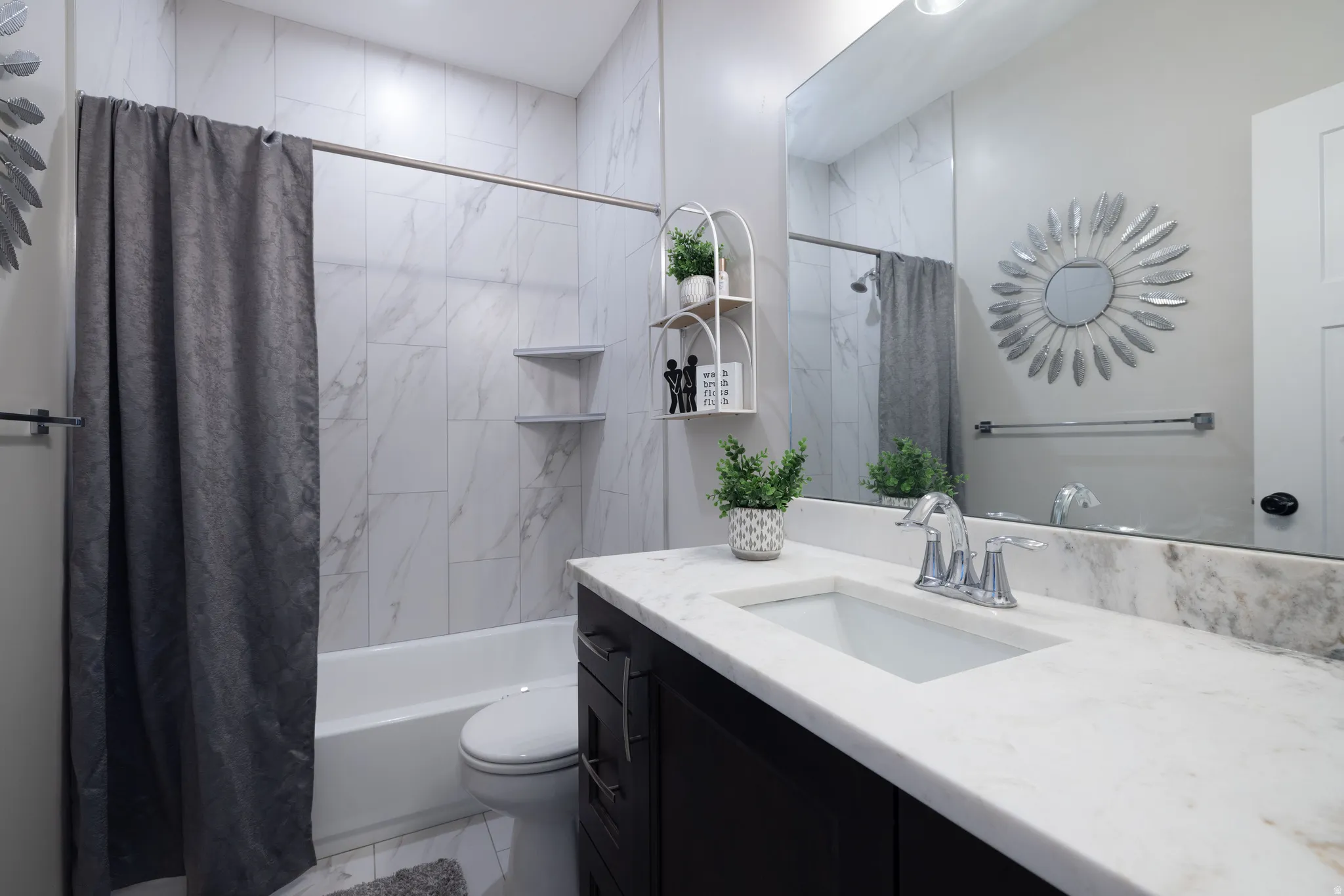 Bathroom featuring a built-in tub and shower combination with white tiled surround, a dark wood-finish vanity with a white countertop, and a single basin sink with chrome fixtures