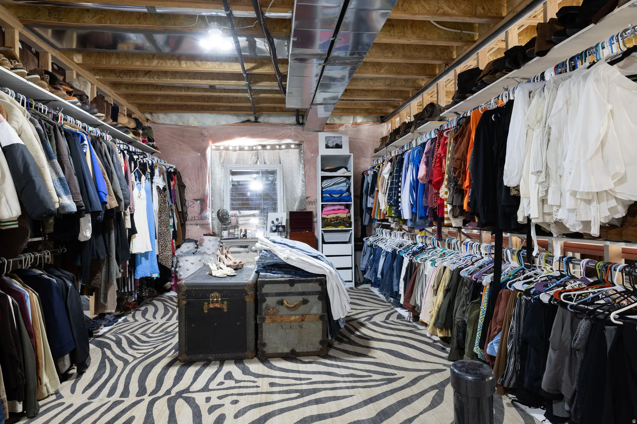Expansive storage area featuring a zebra-patterned carpet, exposed ceiling joists, and multiple garment racks