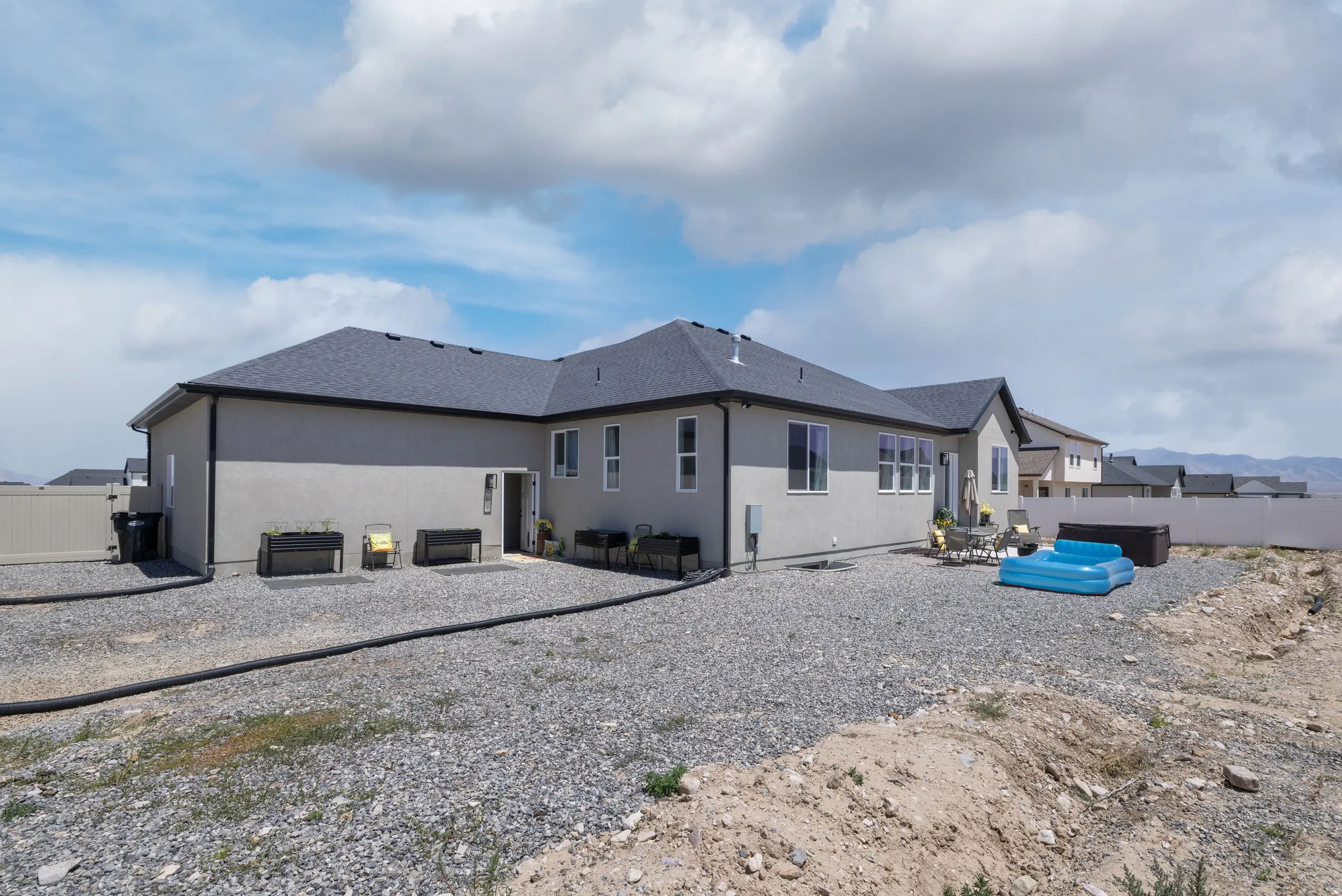 Rear exterior featuring a grey stucco finish, dark shingle roof, and multiple windows