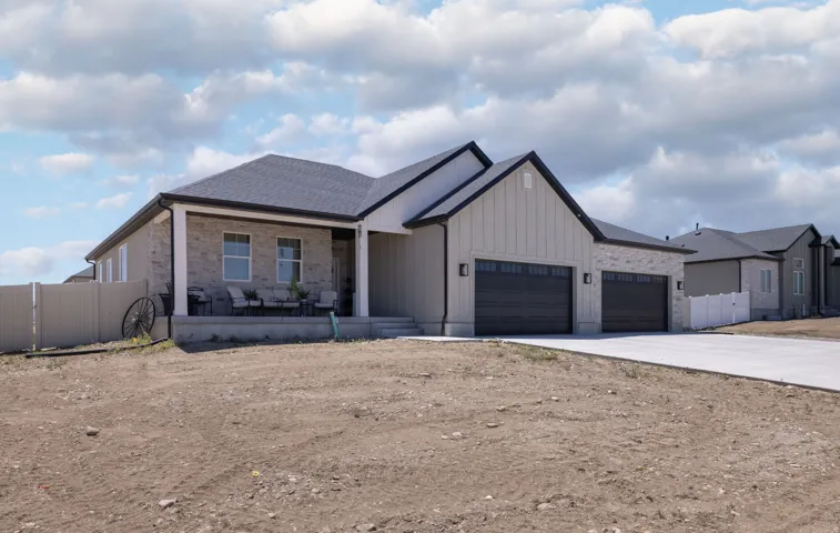 Contemporary ranch-style home featuring a covered front porch, a three-car garage with black carriage-style doors, mixed material facade with light-colored stone, and a dark shingle roof