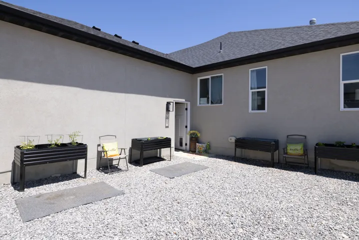 Low-maintenance exterior featuring a gravel patio, stucco siding, and a dark shingle roof