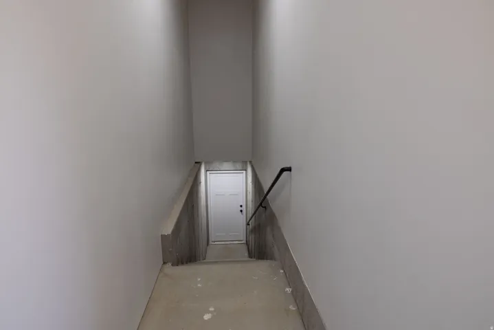 ADU/Basement entrance from Garage.  Stairwell with unfinished concrete steps, a white paneled door, and a black handrail