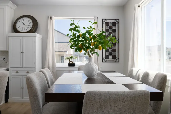 Dining area featuring a dark wood-finish table, light gray upholstered chairs, and a large window with white curtains