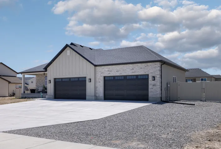 Contemporary exterior featuring a board and batten gable, light-toned stone veneer, and a dark asphalt shingle roof