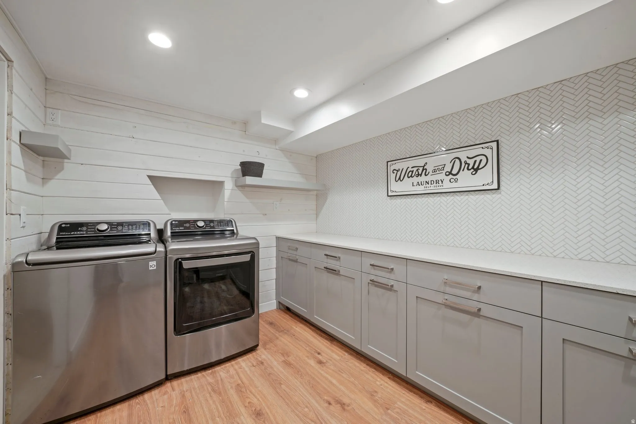 Dedicated laundry space featuring a white shiplap accent wall, wood-finish flooring, recessed lighting, and a herringbone pattern tile backsplash