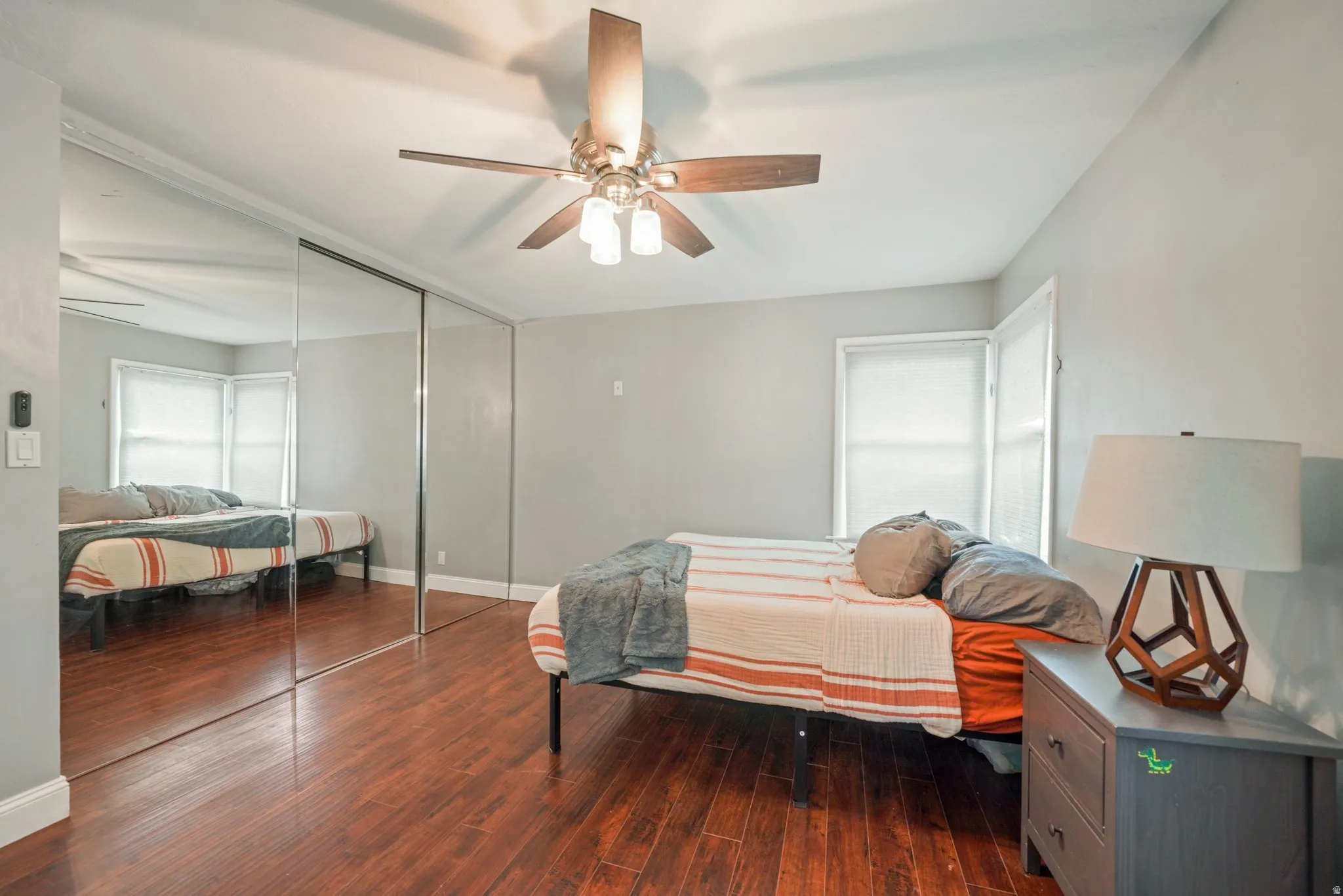 Bedroom featuring wood-finish flooring, a ceiling fan with integrated lighting, and multiple windows with roller shades