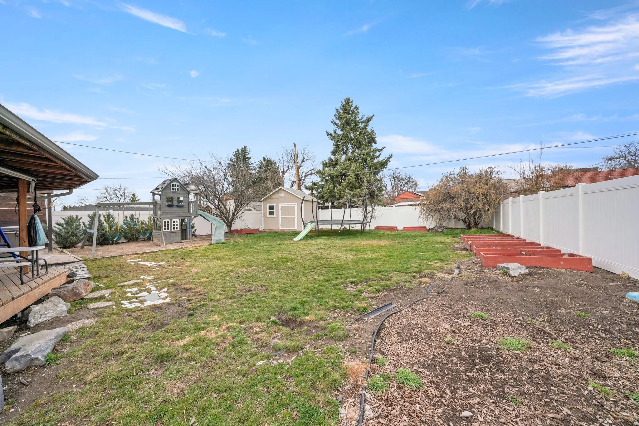 Expansive backyard featuring a deck, a storage shed, a playground and a privacy fence