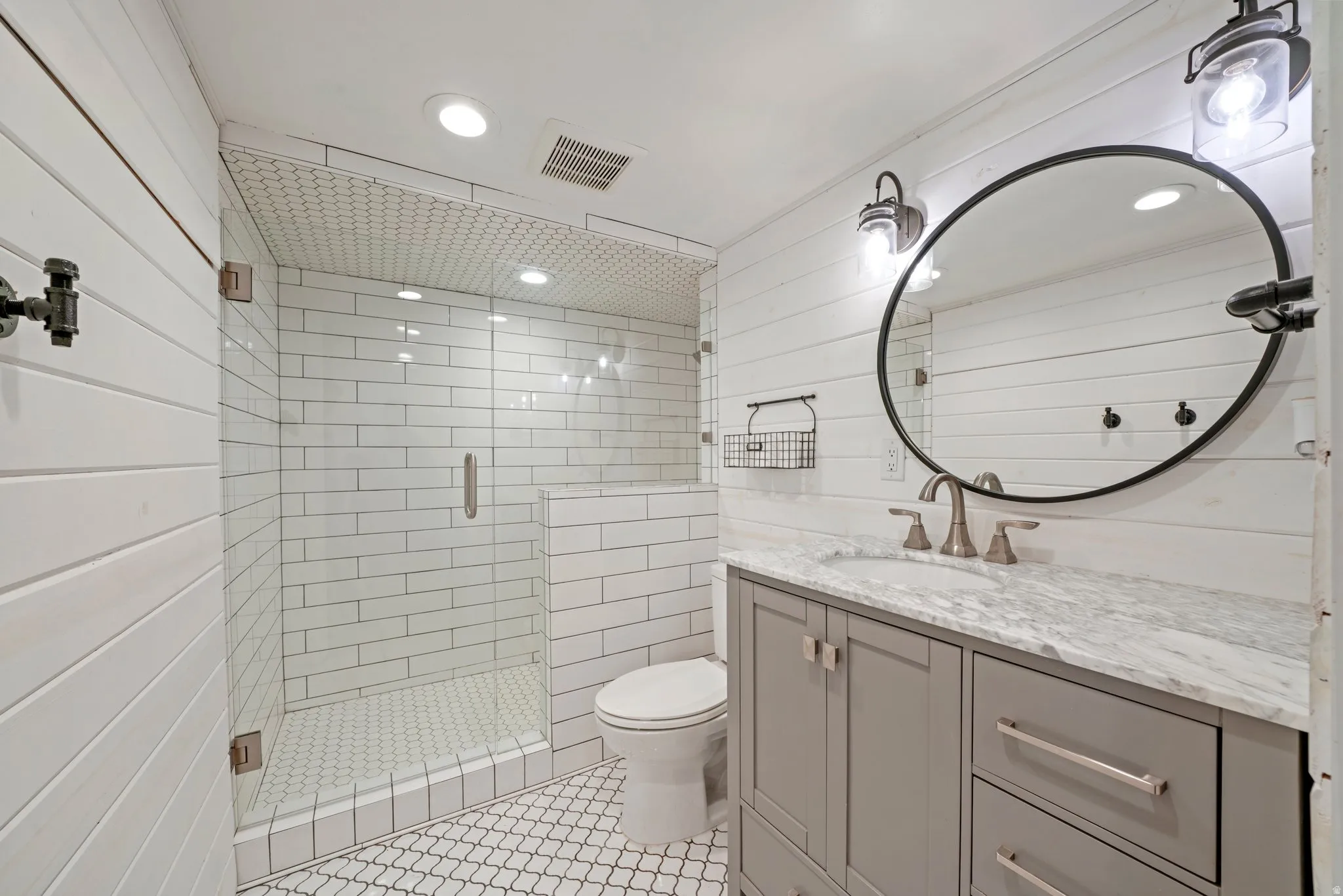 Bathroom featuring a glass-enclosed shower with subway tile surround, shiplap wall finishes, a vanity with a stone countertop, and decorative mirror