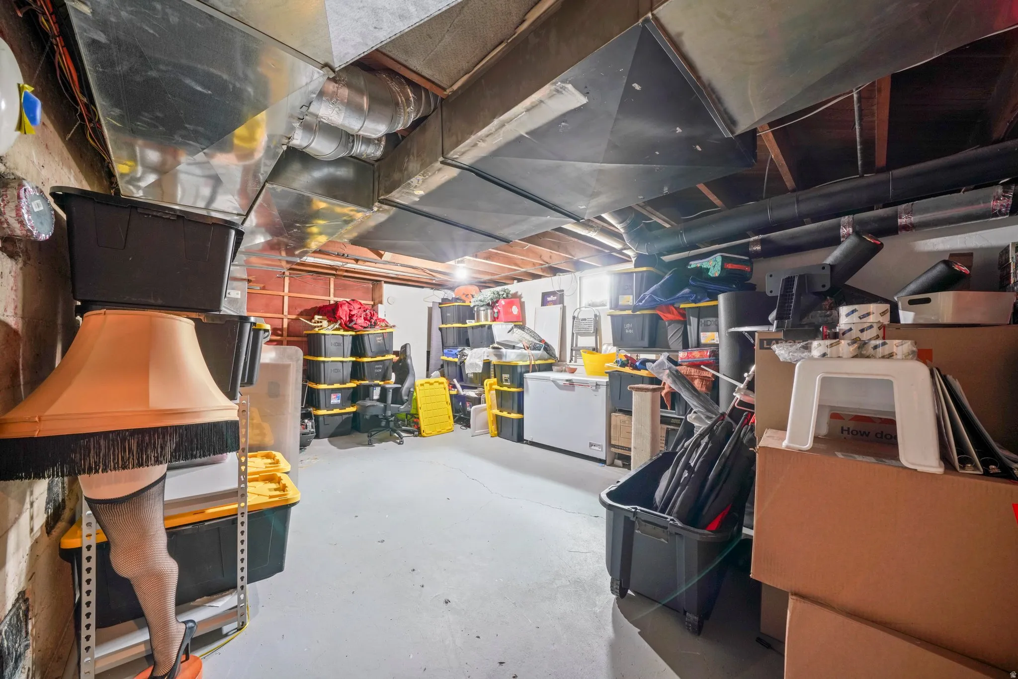 Unfinished basement with exposed ceiling beams and ductwork, concrete flooring, and ample storage space