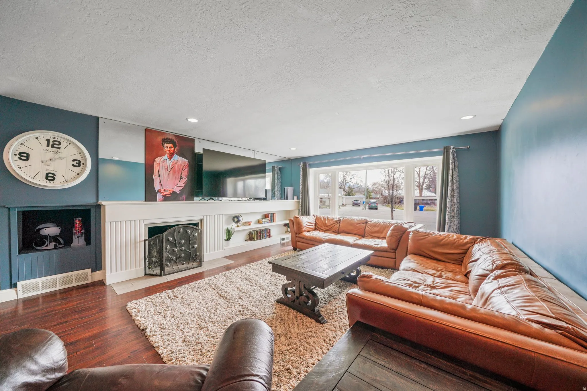 Spacious living area featuring rich wood-finish flooring, a prominent fireplace with a decorative screen, and extensive built-in shelving