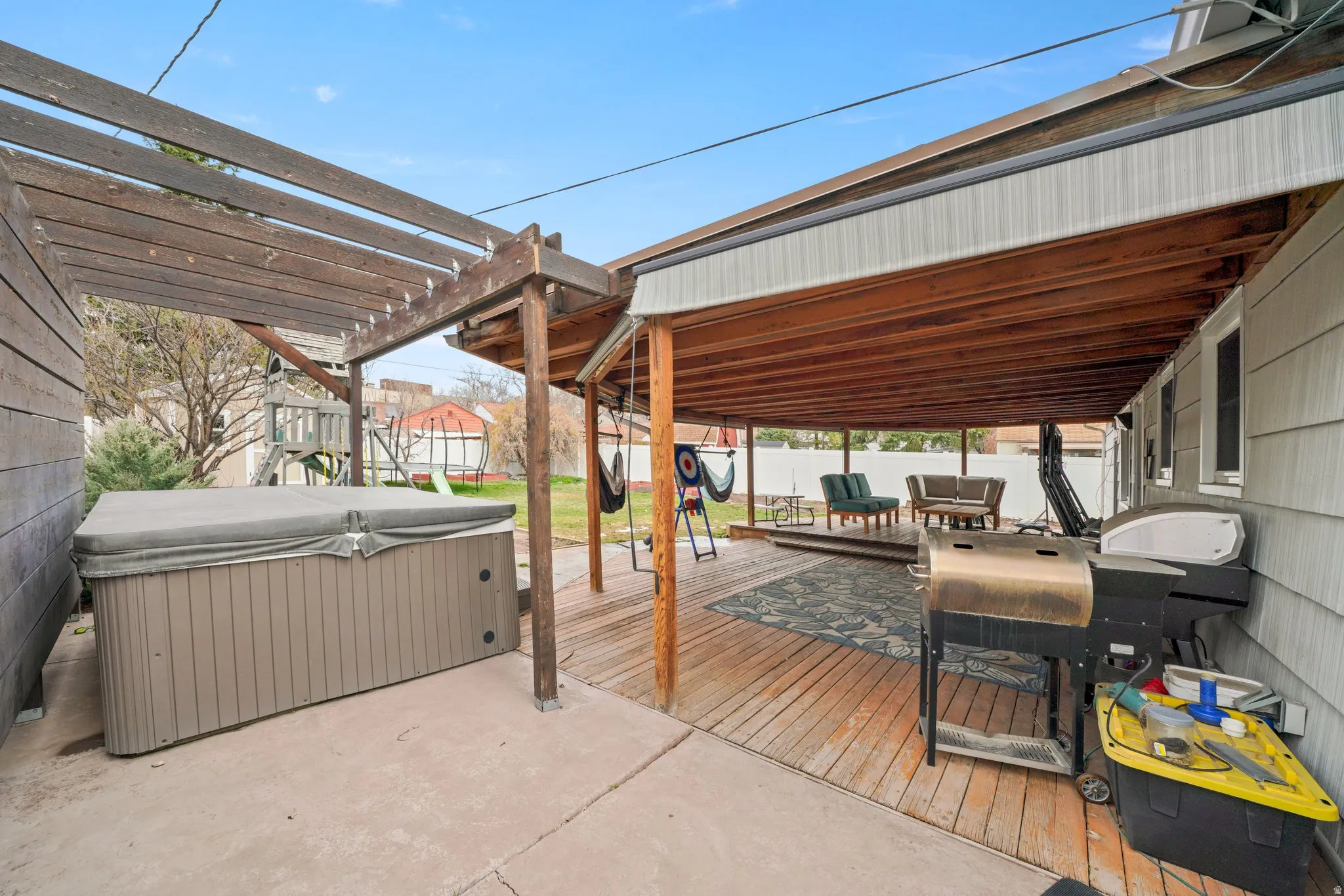 Expansive backyard featuring a covered deck, wood-finish decking, and a hot tub.
