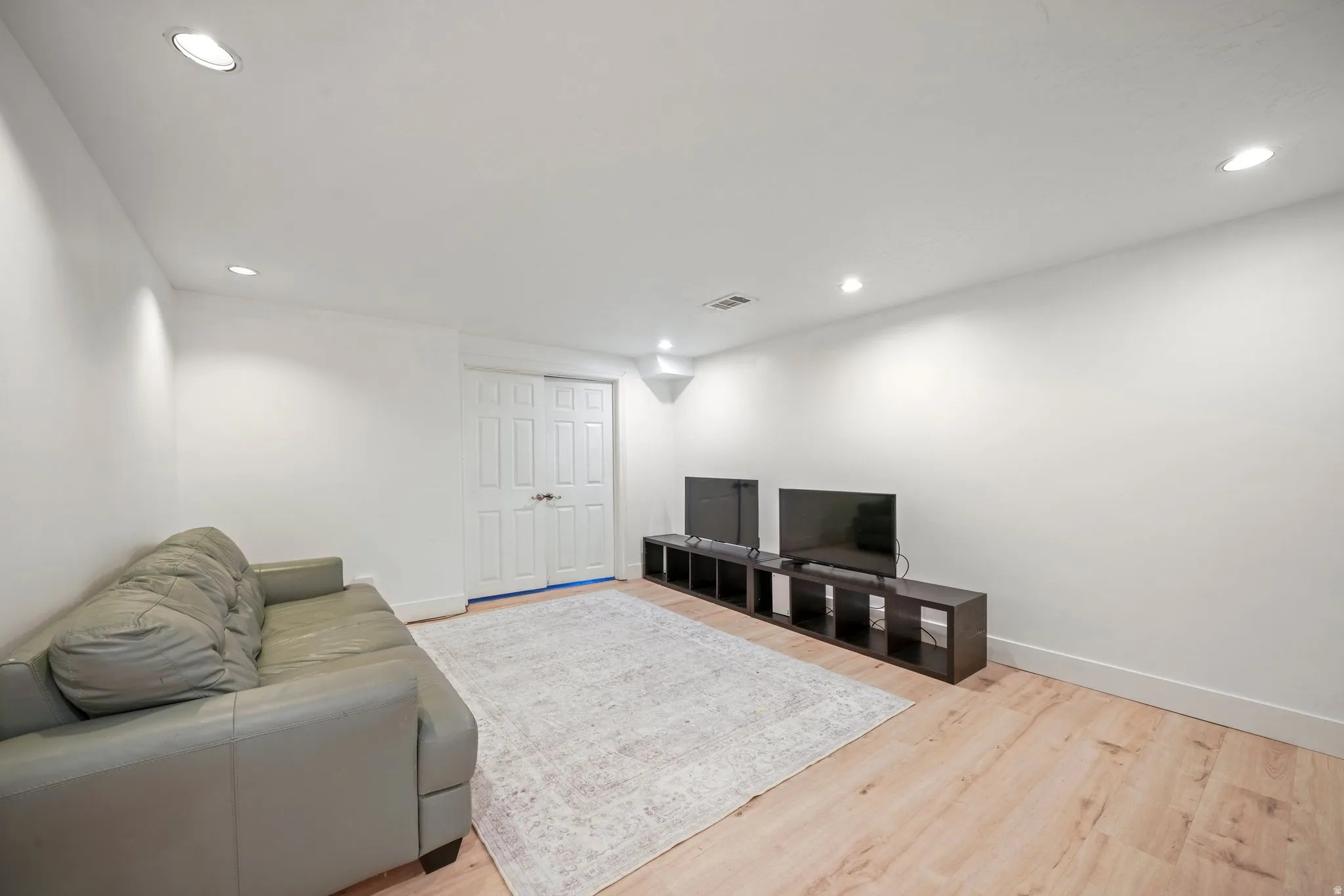 Recessed lighting illuminates this room, featuring light wood-finish flooring and white baseboards