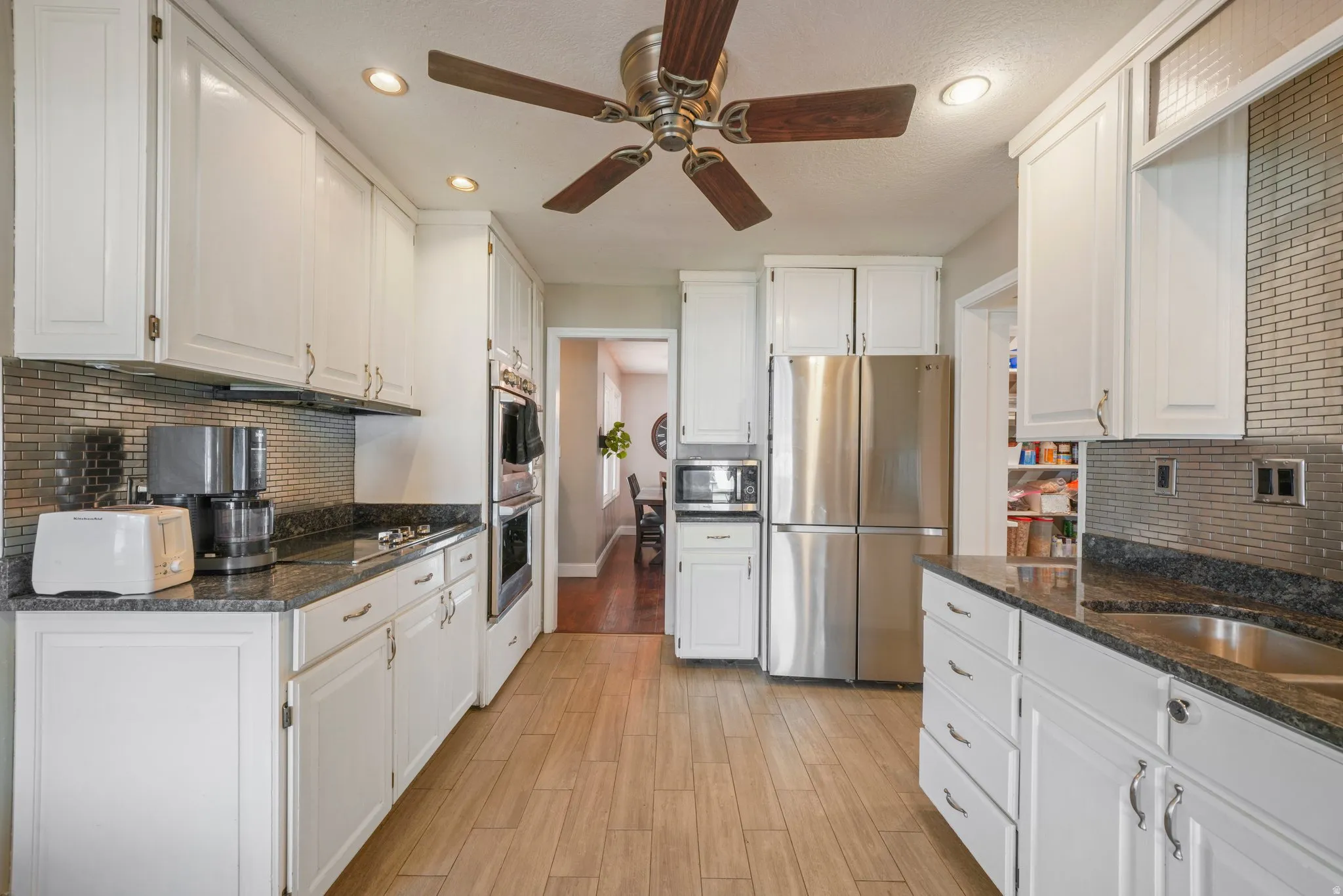 Kitchen featuring white cabinetry, dark stone countertops, stainless steel appliances, a tiled backsplash, and wood-finish flooring