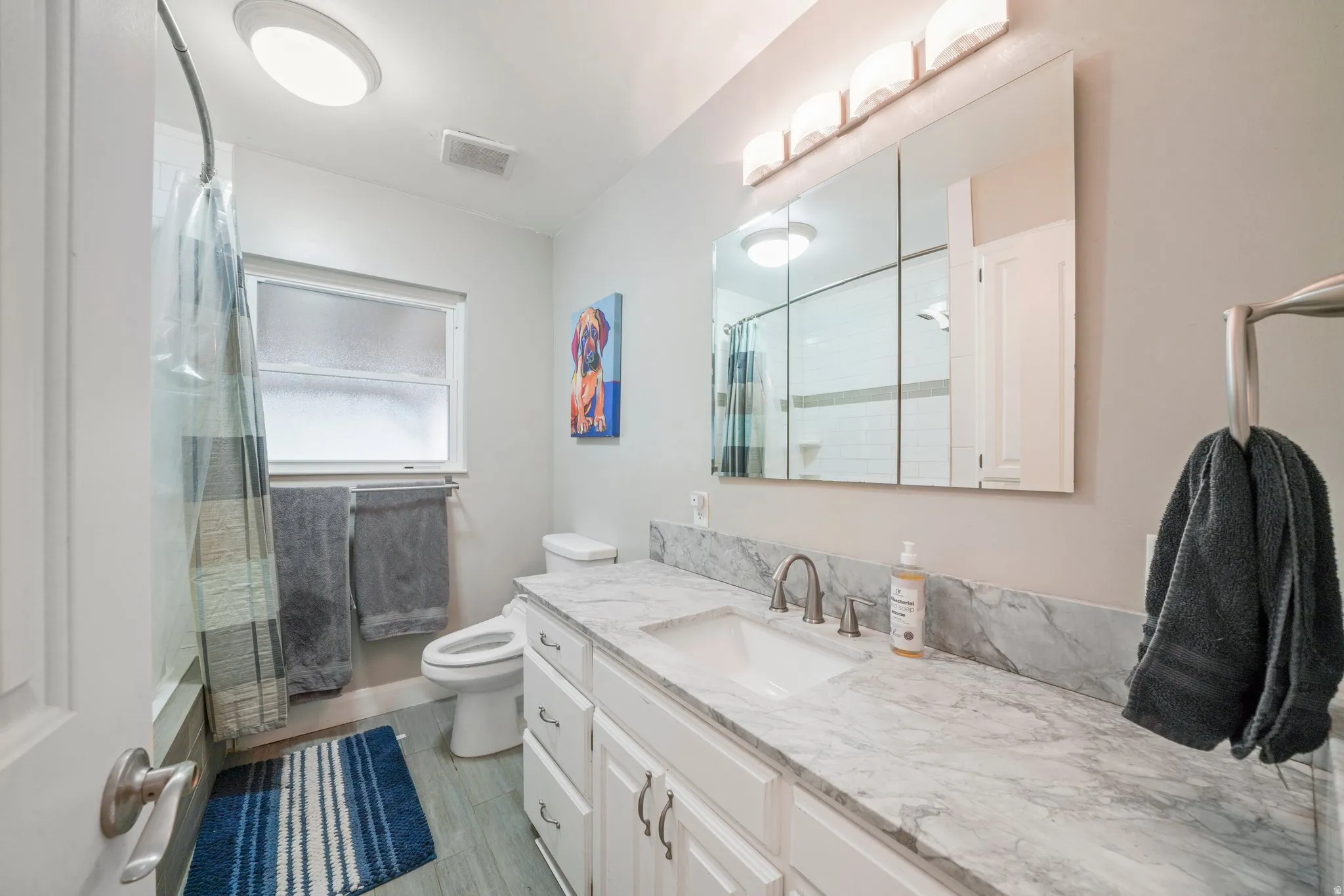 Bright bathroom featuring a white vanity with an integrated sink, a gray marbled countertop, and a mirrored medicine cabinet