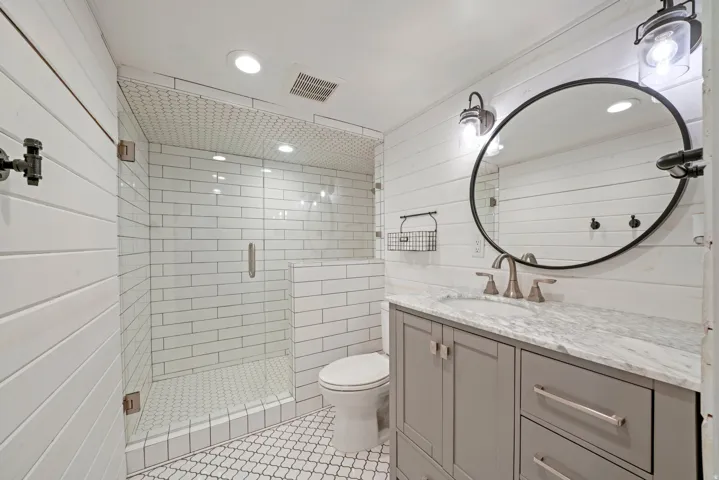 Bathroom featuring a glass-enclosed shower with subway tile surround, shiplap wall finishes, a vanity with a stone countertop, and decorative mirror