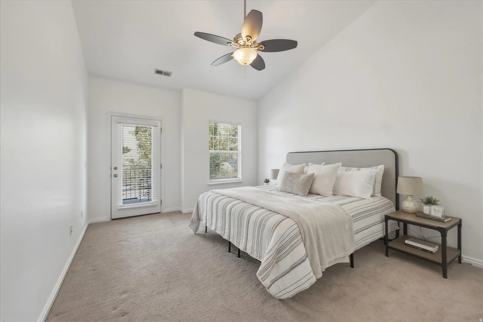 Vaulted ceiling room featuring light-colored carpeting, a ceiling fan with integrated lighting, a full-light exterior door with blinds, and a window with blinds