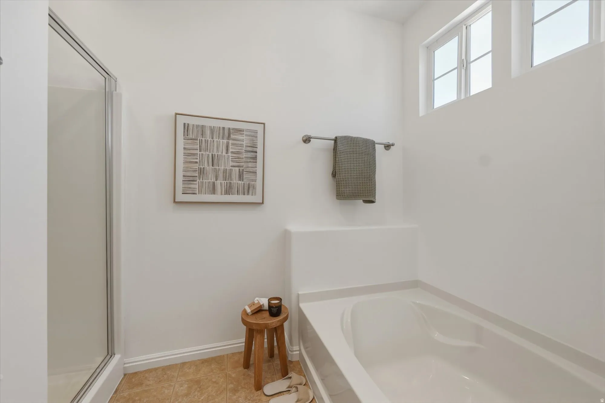 White-walled bathroom featuring a built-in bathtub, glass-enclosed shower, light-colored floor tiles, and high-set windows