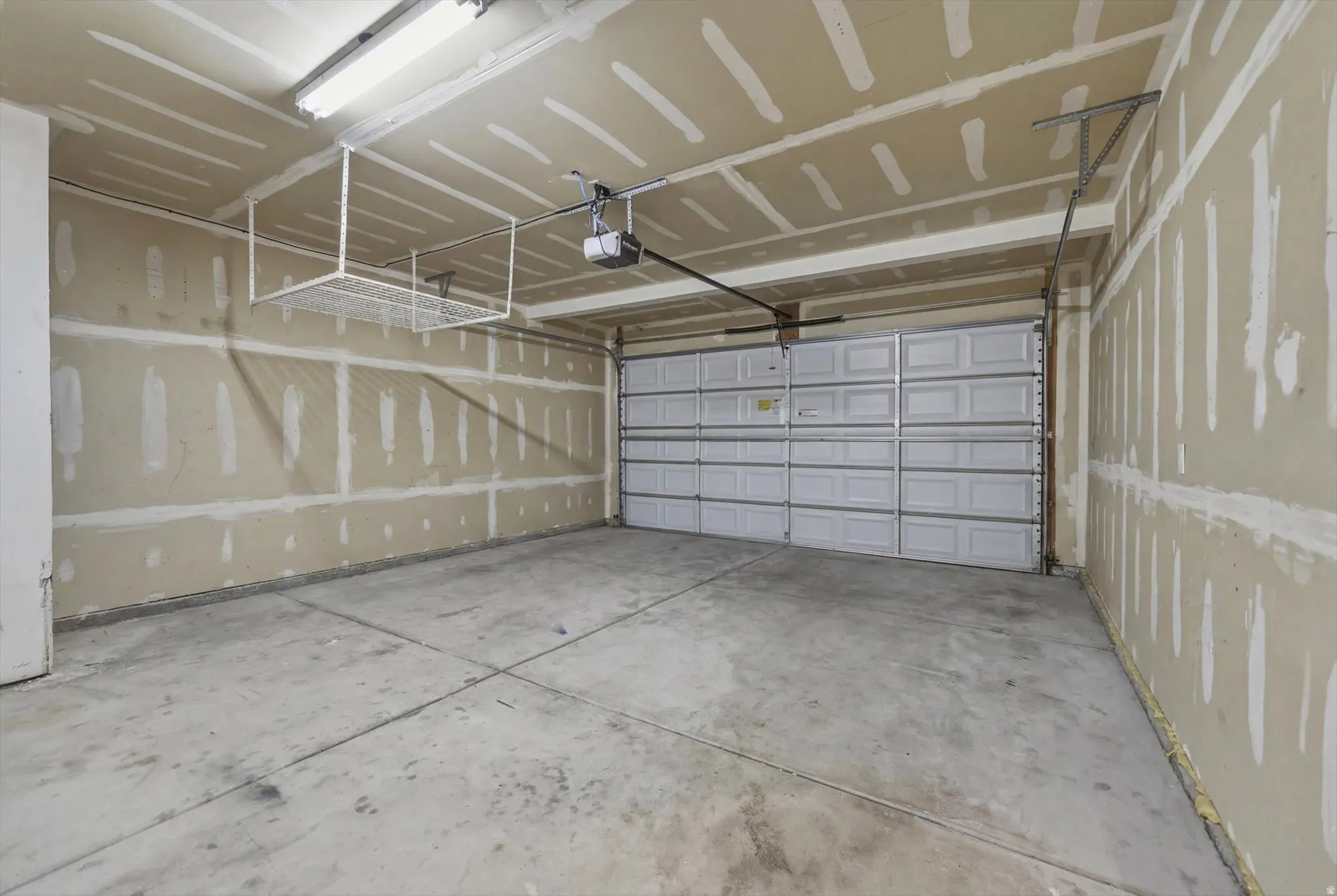 Spacious garage featuring a paneled garage door, exposed drywall, concrete flooring, overhead fluorescent lighting, and an overhead storage rack