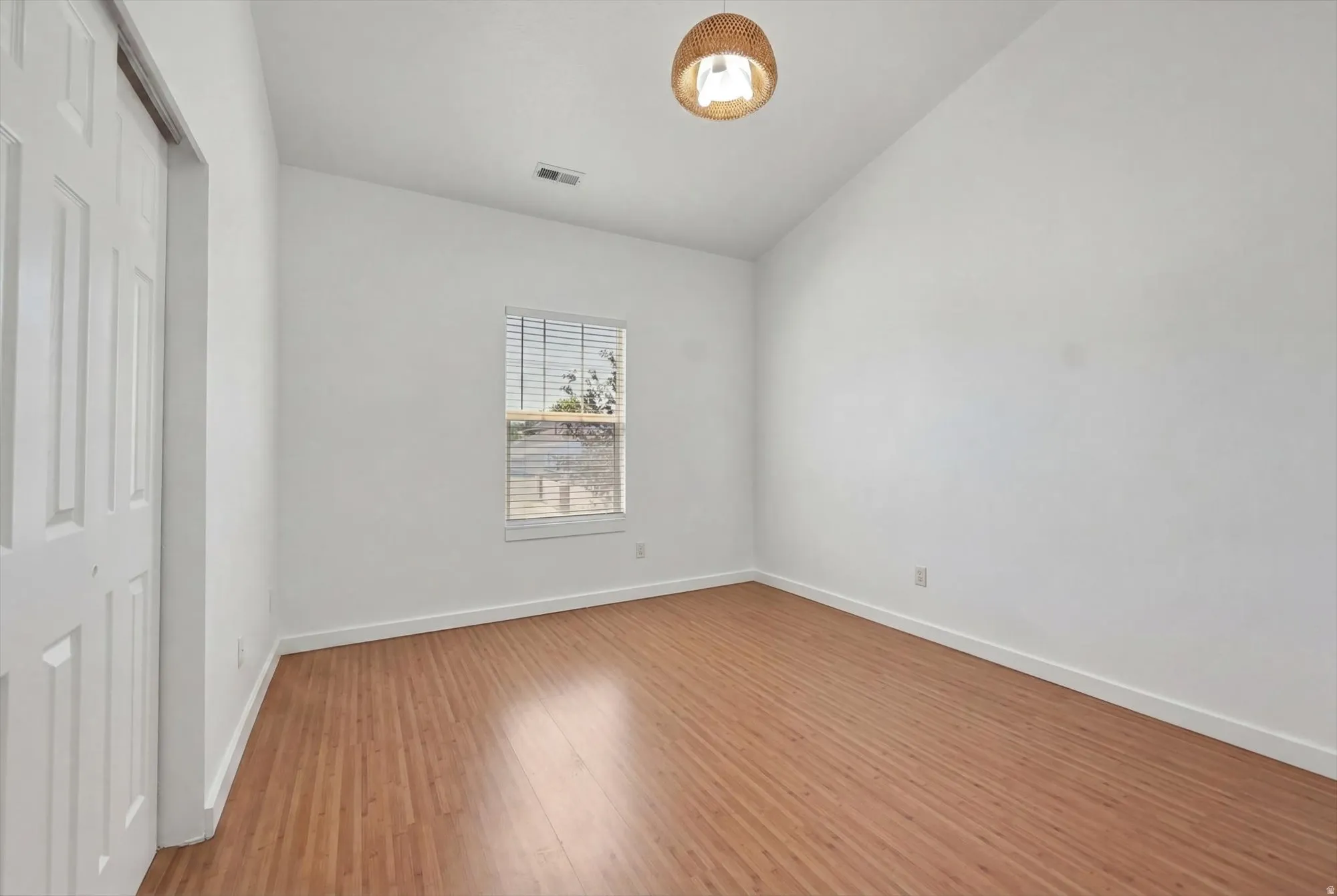 Room featuring wood-finish flooring, white baseboards, a single window with blinds, and a built-in closet with bifold doors