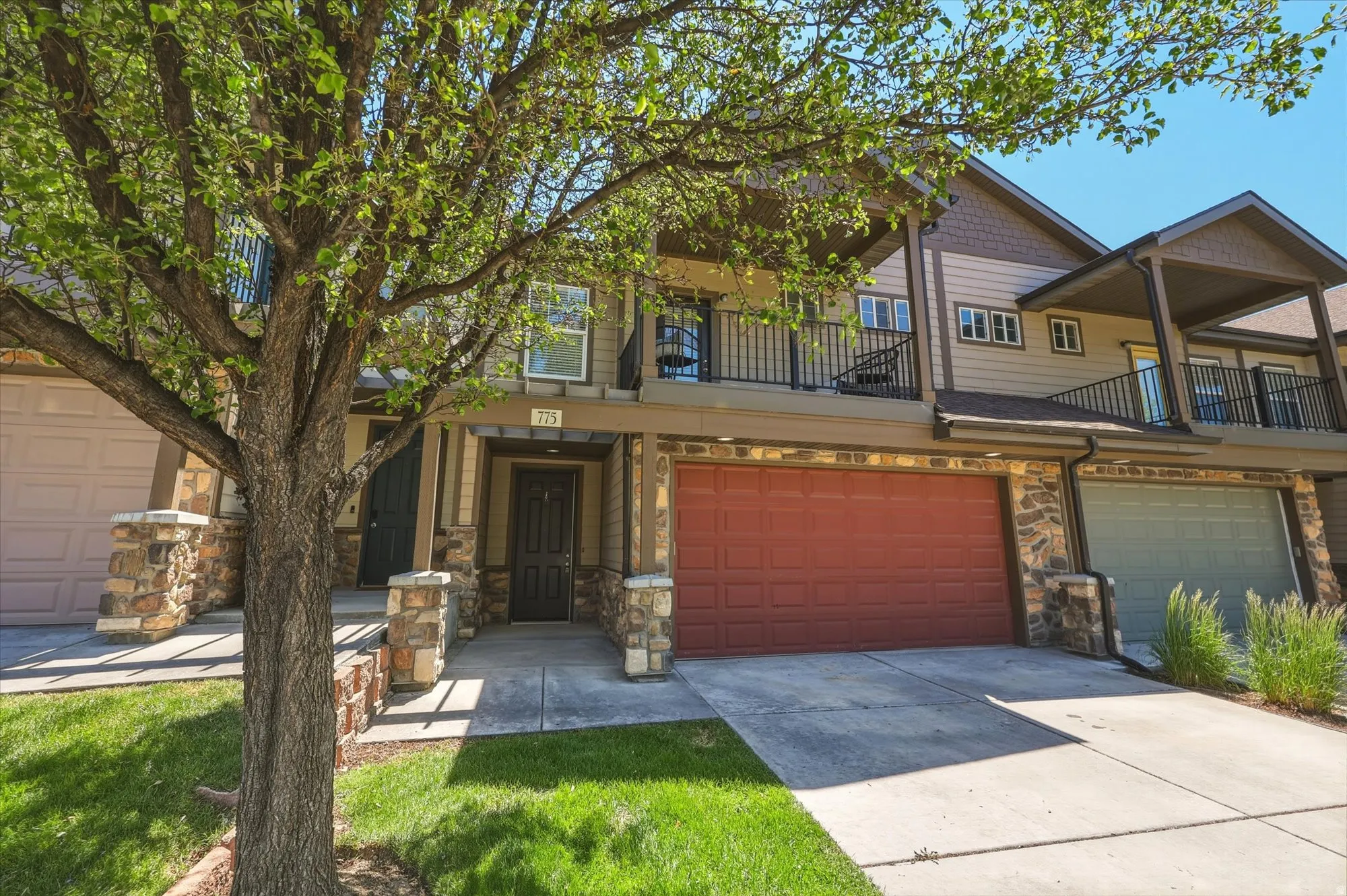 Modern townhome exterior featuring an attached garage with a red door, stone facade accents, and a second-story balcony with dark railings