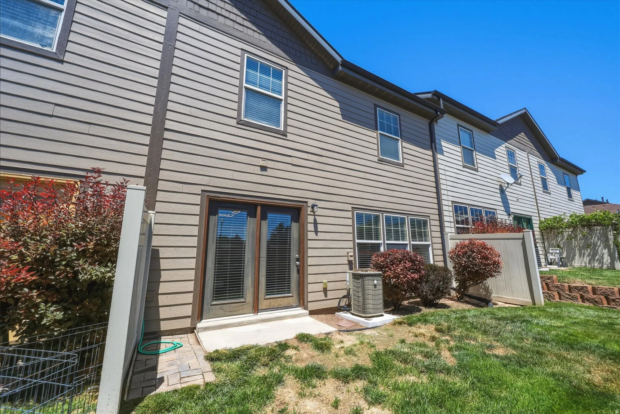 Private fenced yard featuring a concrete patio, double glass doors, and mature landscaping