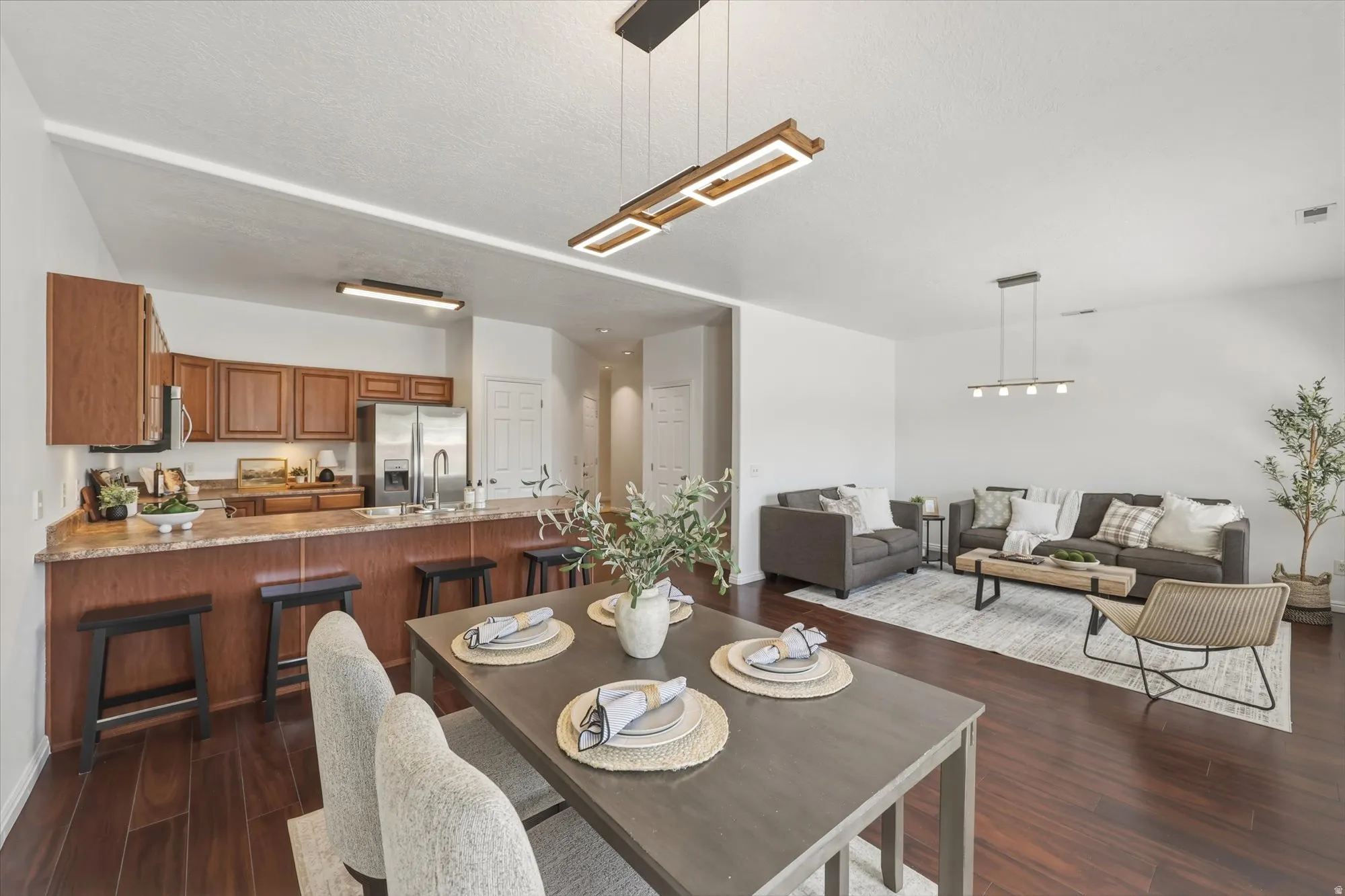Open-concept living space featuring wood-finish flooring, a kitchen with stainless steel appliances, a breakfast bar, and contemporary lighting fixtures