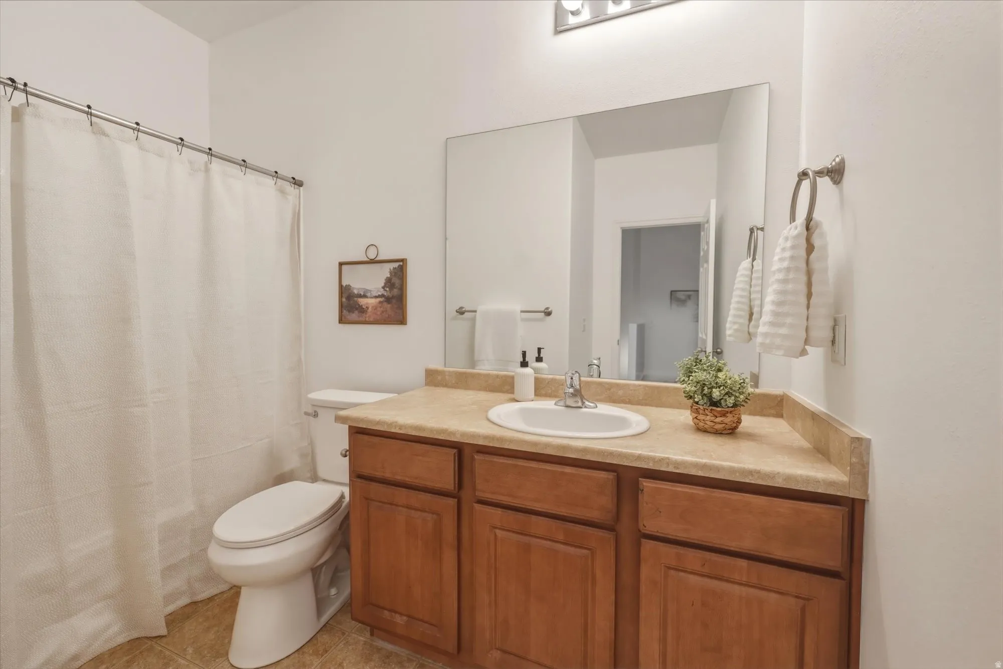 Full bathroom featuring a single vanity with wood-finish cabinetry and a light-toned countertop, a large wall-mounted mirror, and a toilet