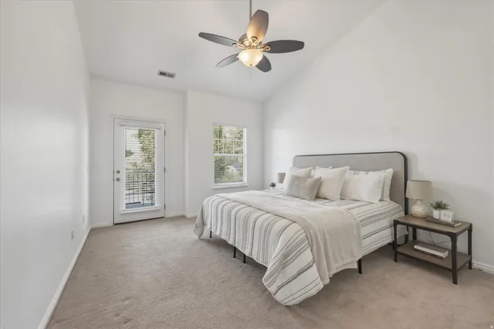 Vaulted ceiling room featuring light-colored carpeting, a ceiling fan with integrated lighting, a full-light exterior door with blinds, and a window with blinds