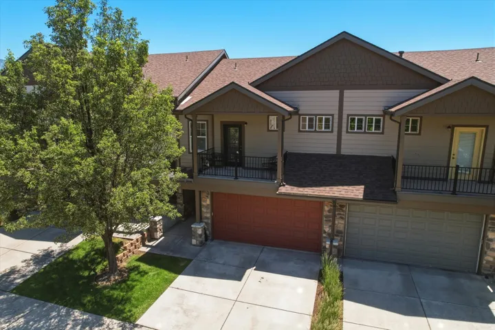 Multi-level townhome featuring a neutral-toned exterior with brown trim accents, shingle roofing, and a prominent red garage door