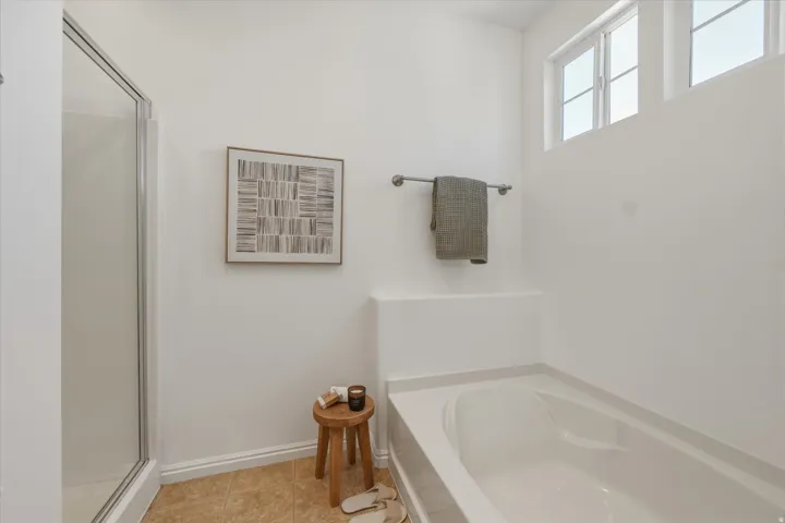 White-walled bathroom featuring a built-in bathtub, glass-enclosed shower, light-colored floor tiles, and high-set windows