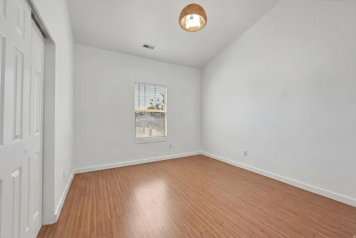 Room featuring wood-finish flooring, white baseboards, a single window with blinds, and a built-in closet with bifold doors