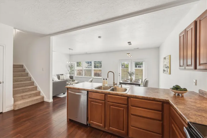Kitchen island featuring a double-basin stainless steel sink with a high-arc faucet, rich wood cabinetry, and a stainless steel dishwasher