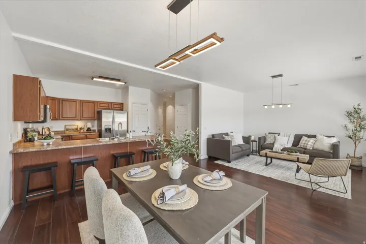 Open-concept living space featuring wood-finish flooring, a kitchen with stainless steel appliances, a breakfast bar, and contemporary lighting fixtures
