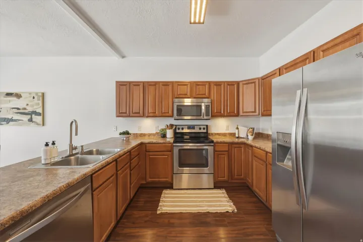 Kitchen featuring wood-finish cabinetry, stainless steel appliances, a double basin sink, and wood-finish flooring