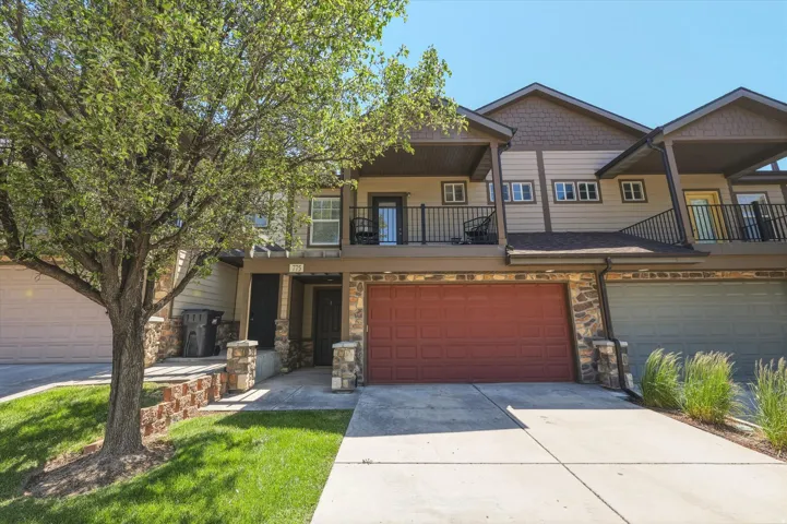 Multi-level townhome exterior featuring an attached garage, stone accents, and a second-story balcony