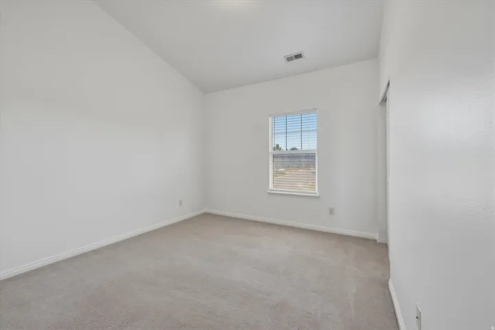 Bedroom featuring vaulted ceilings, neutral carpeting, and a window with horizontal blinds
