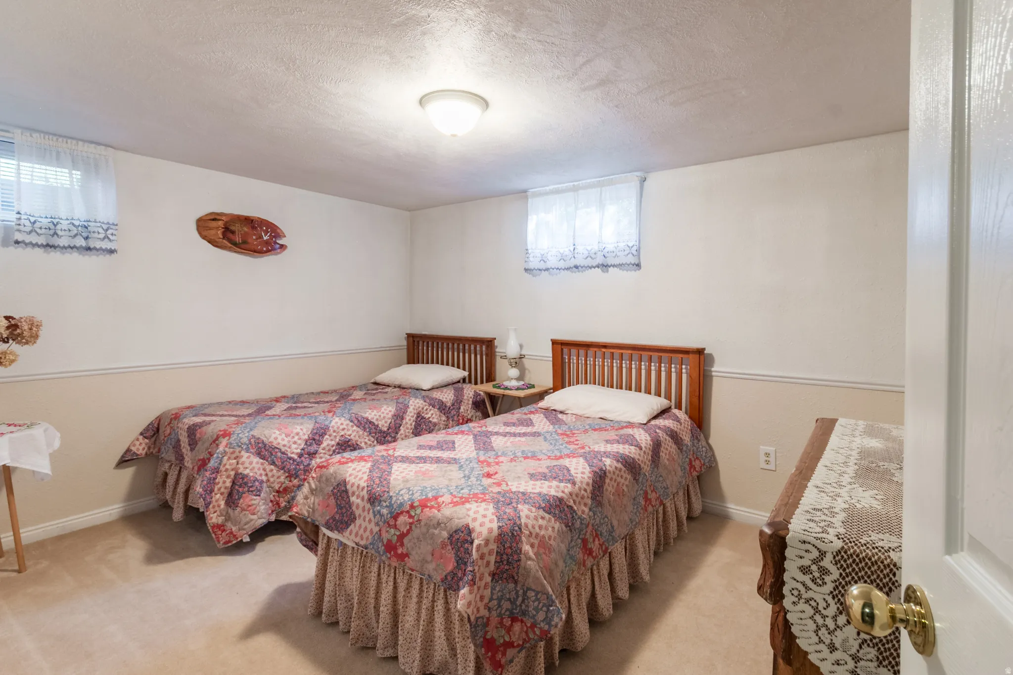 Carpeted room featuring two wood-frame beds, painted walls with wainscoting, and a ceiling-mounted light fixture