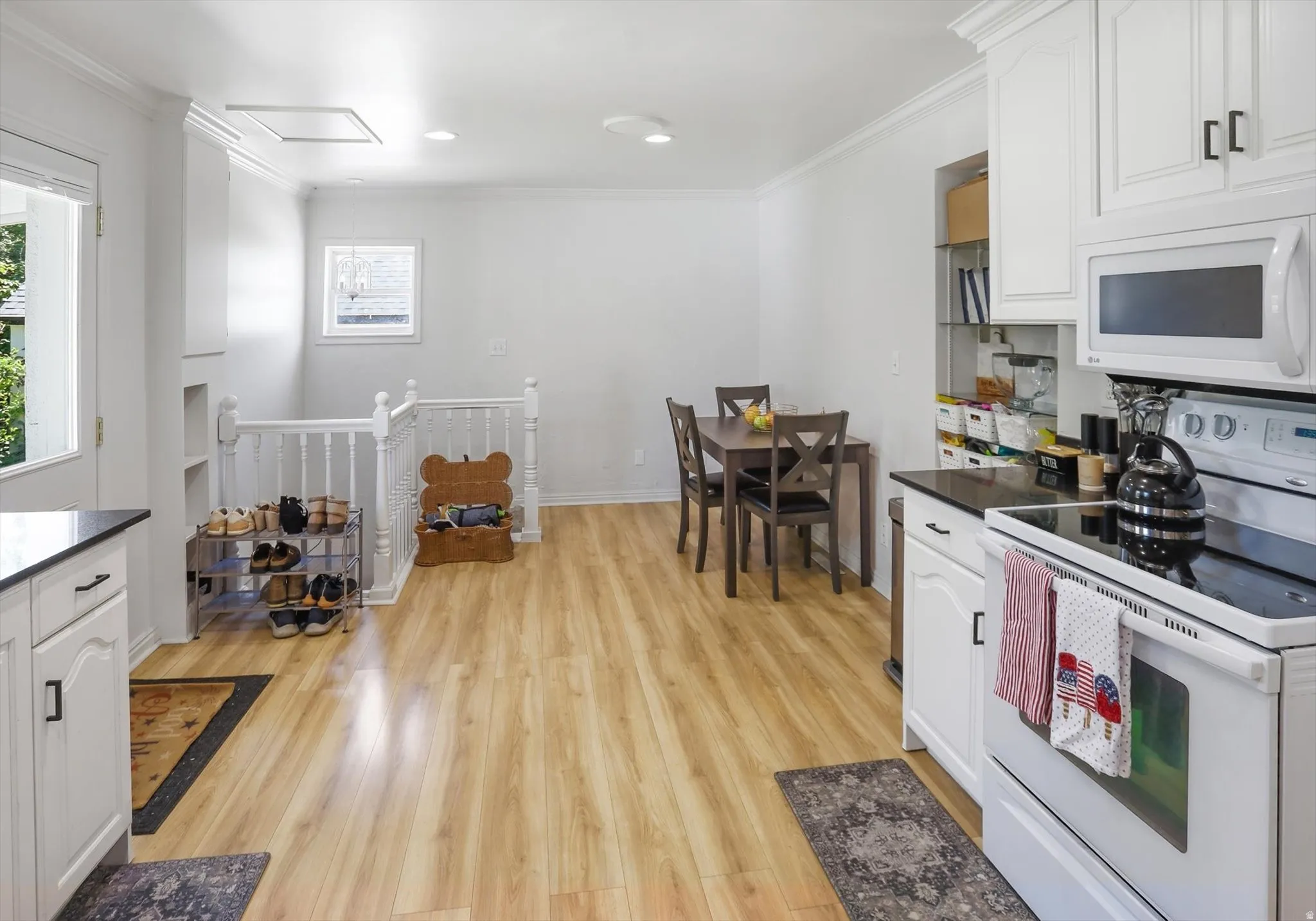 Open-concept kitchen and dining area featuring light wood-finish flooring, white cabinetry with dark hardware, dark countertops, and a full suite of white appliances