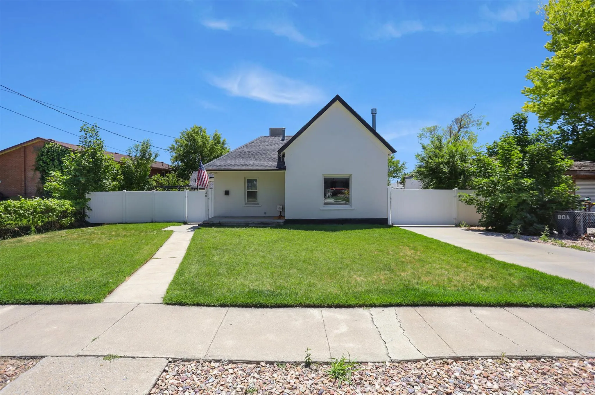 White stucco residence with a dark shingle roof, featuring a concrete front walkway and a white privacy fence
