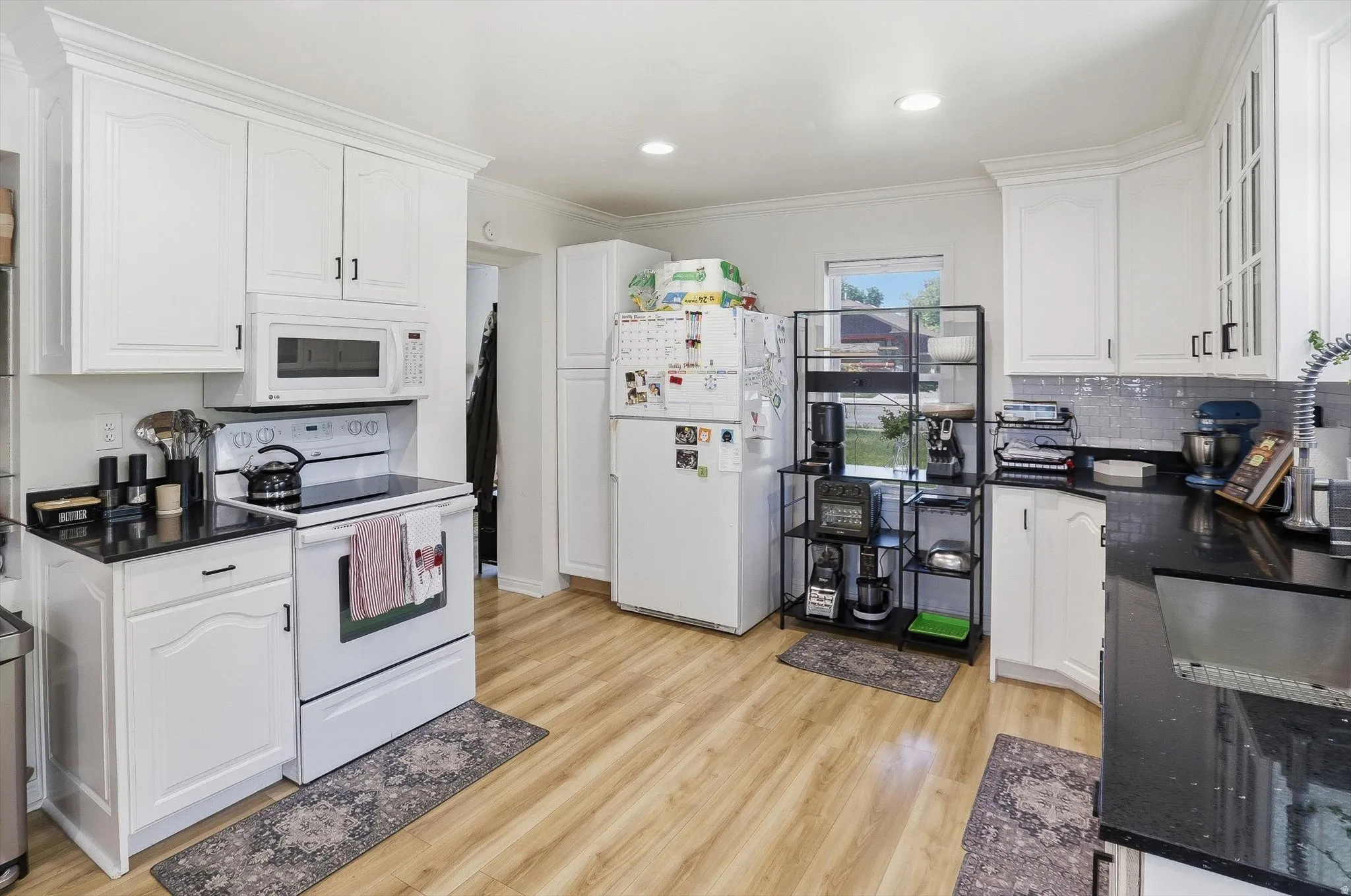 Bright kitchen featuring white cabinetry, dark countertops, wood-finish flooring, a white range, and a tile backsplash