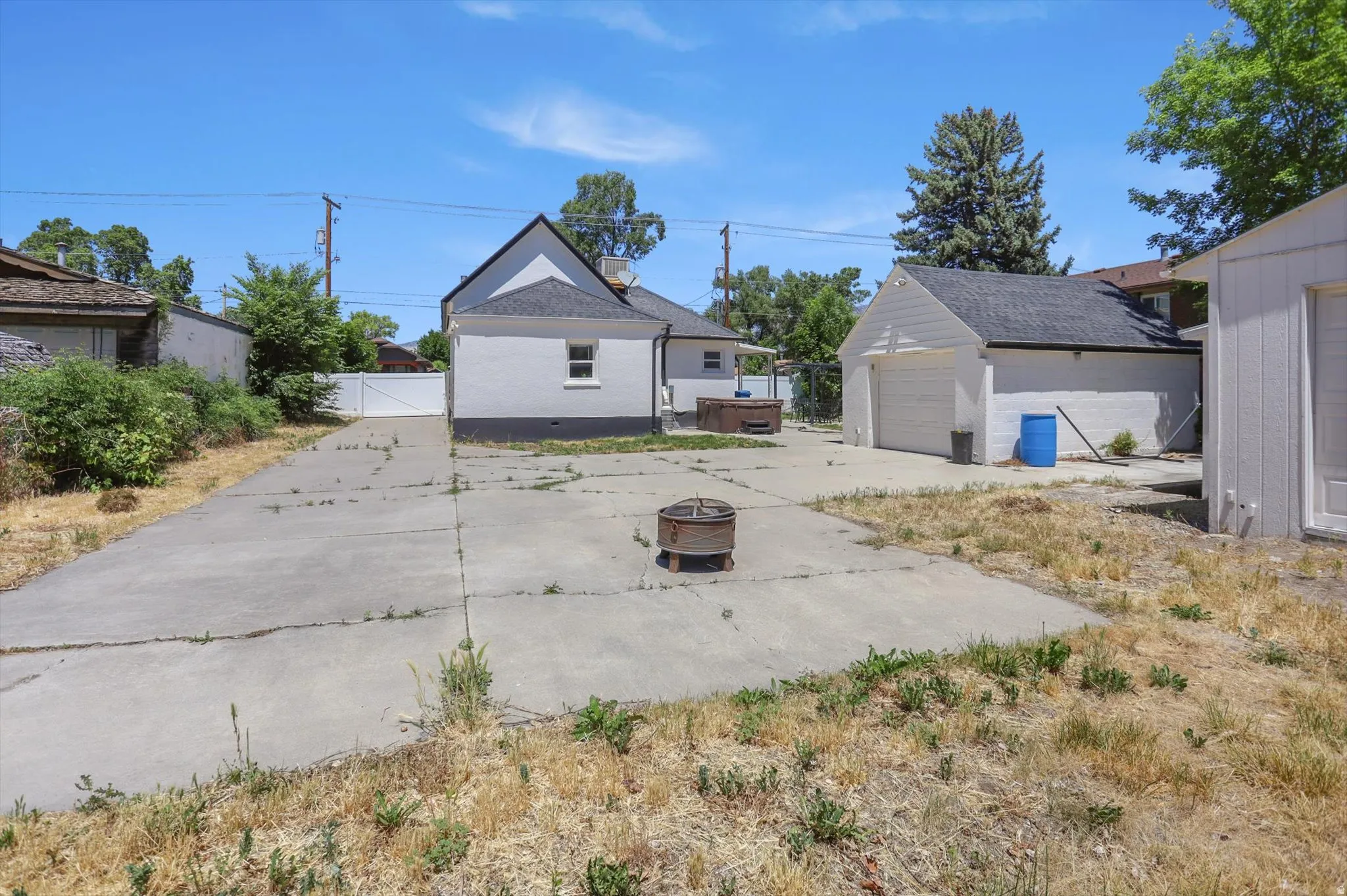 Expansive concrete patio with a detached garage and additional outbuilding, featuring a white privacy fence