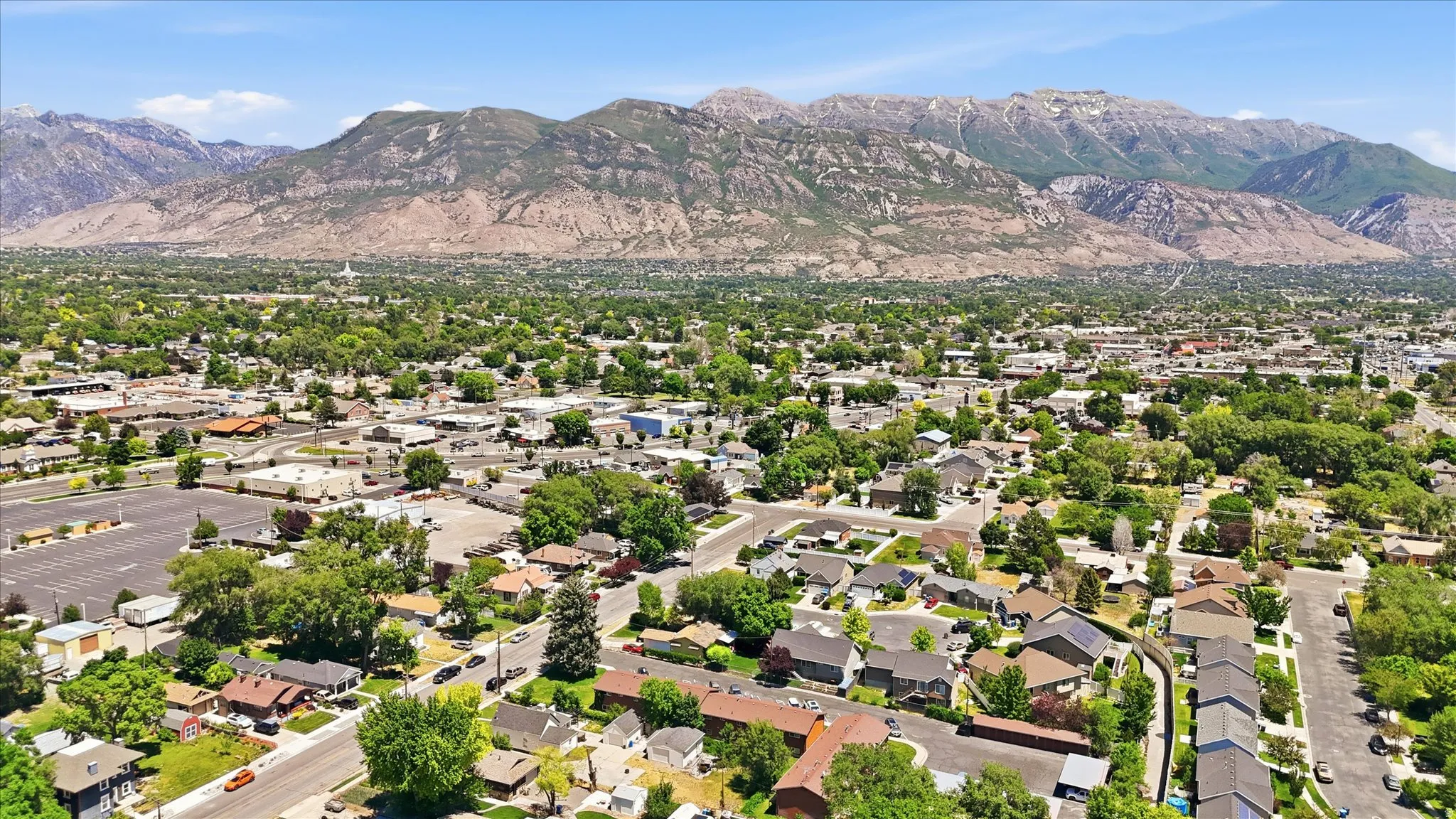 Expansive aerial landscape featuring a residential neighborhood with mature trees, commercial areas, and mountain backdrops