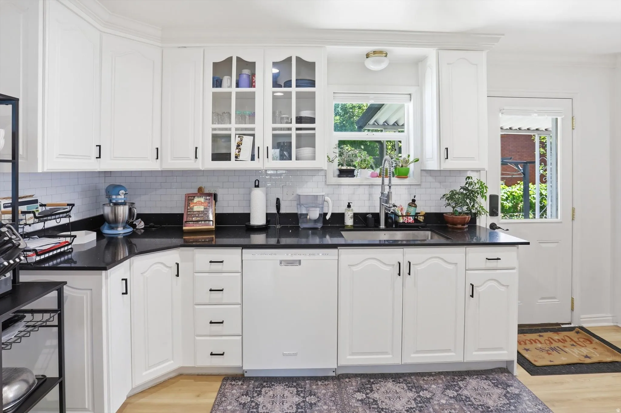 White cabinetry with black hardware, dark countertops, subway tile backsplash, and a stainless steel sink with a gooseneck faucet