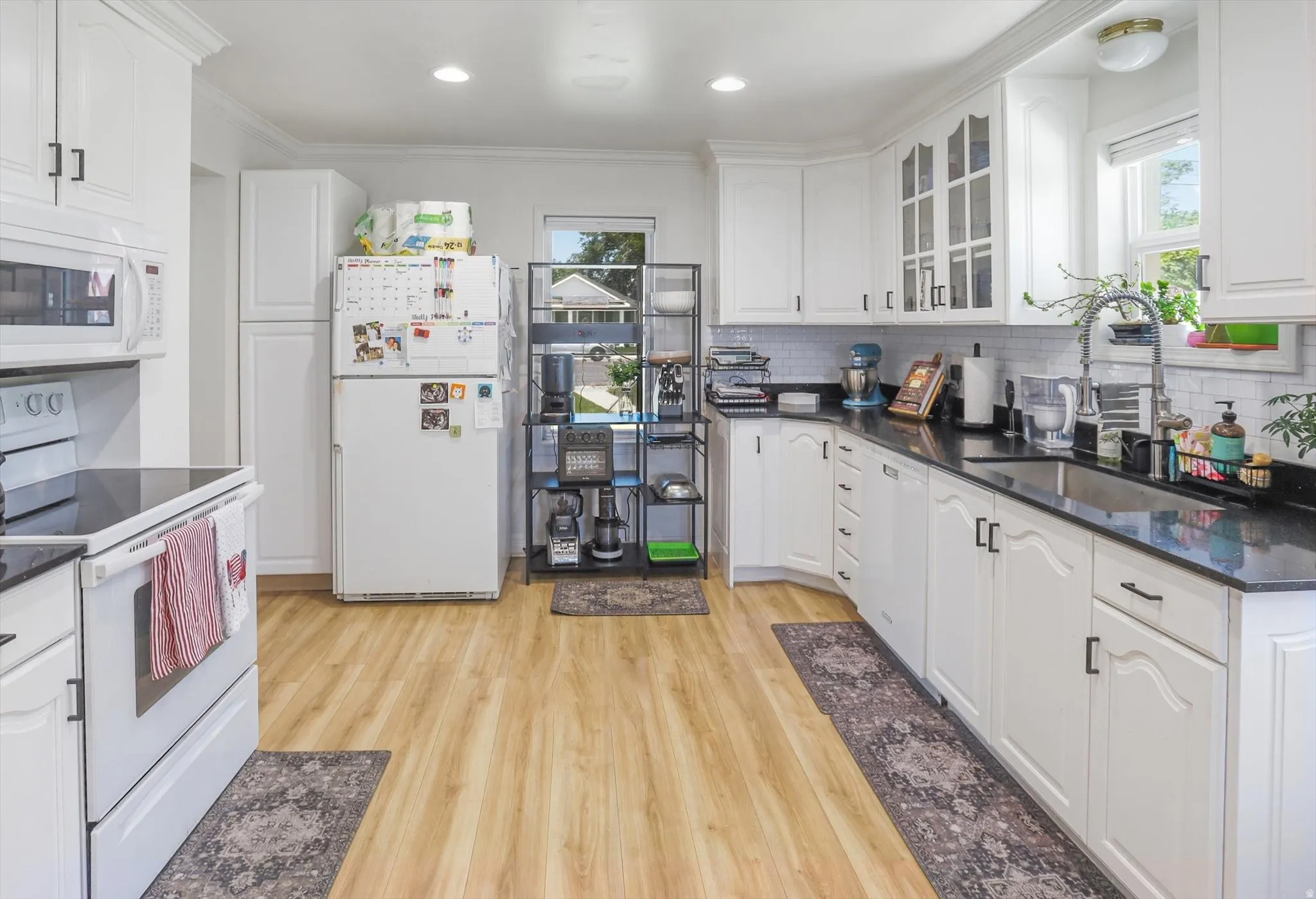 Kitchen featuring white cabinetry, black countertops, stainless steel sink with gooseneck faucet, light wood-finish flooring, and white subway tile backsplash