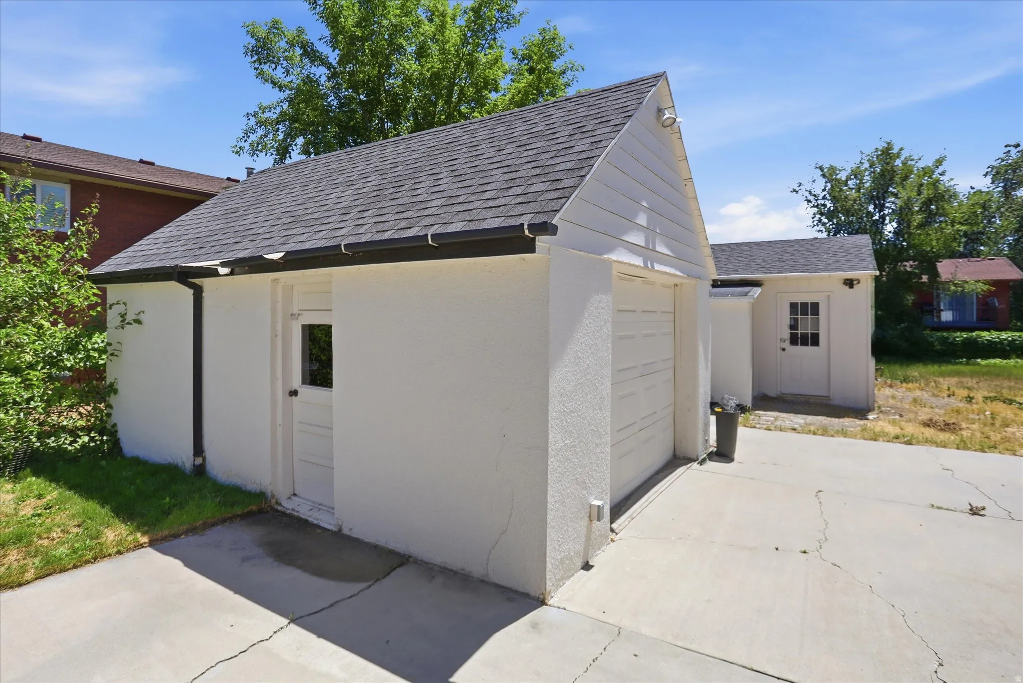 Detached garage structure with white stucco exterior and a dark shingle roof