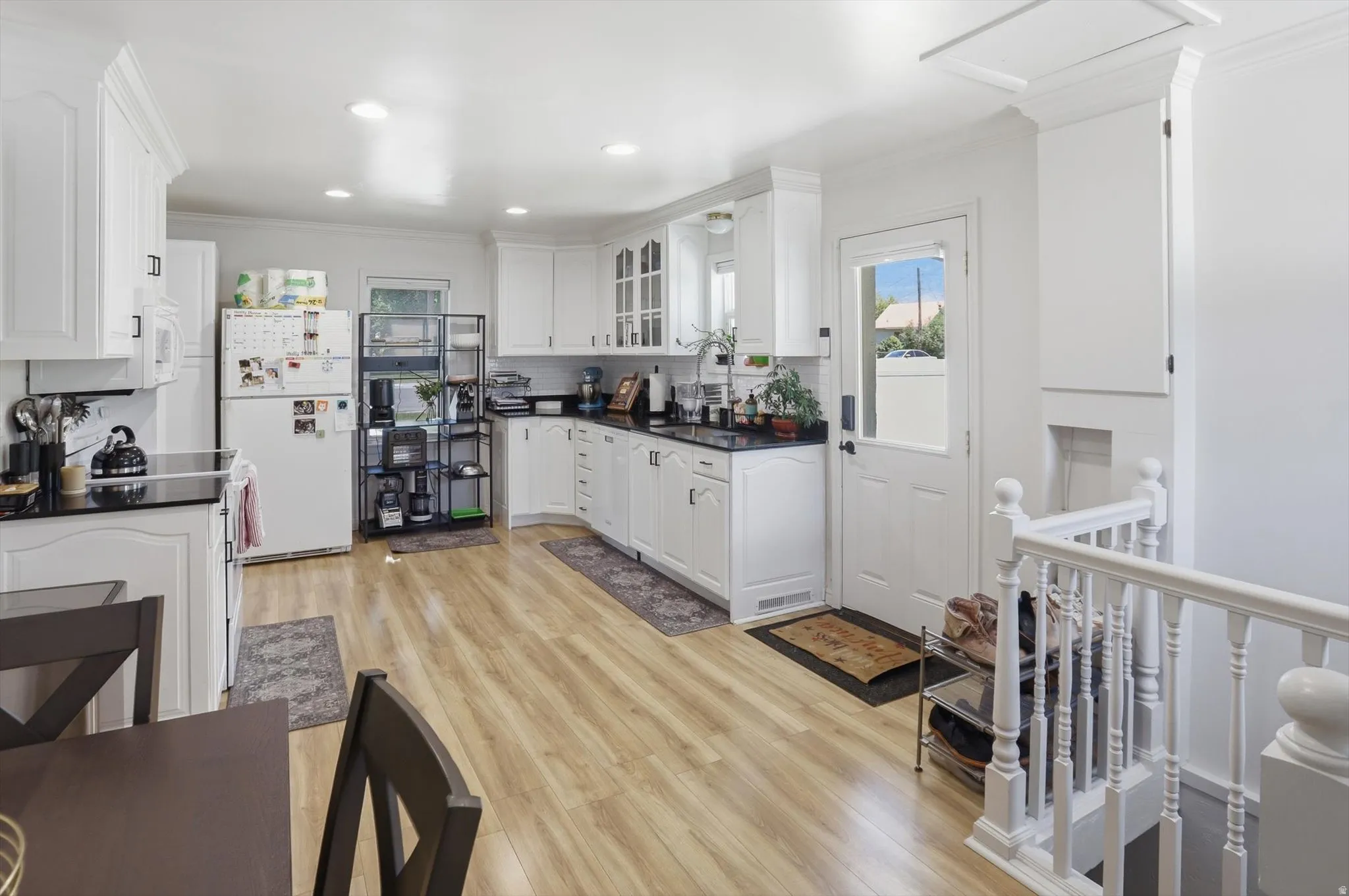 Bright kitchen featuring white cabinetry, dark countertops, wood-finish flooring, recessed lighting, and a partially glass-paned exterior door