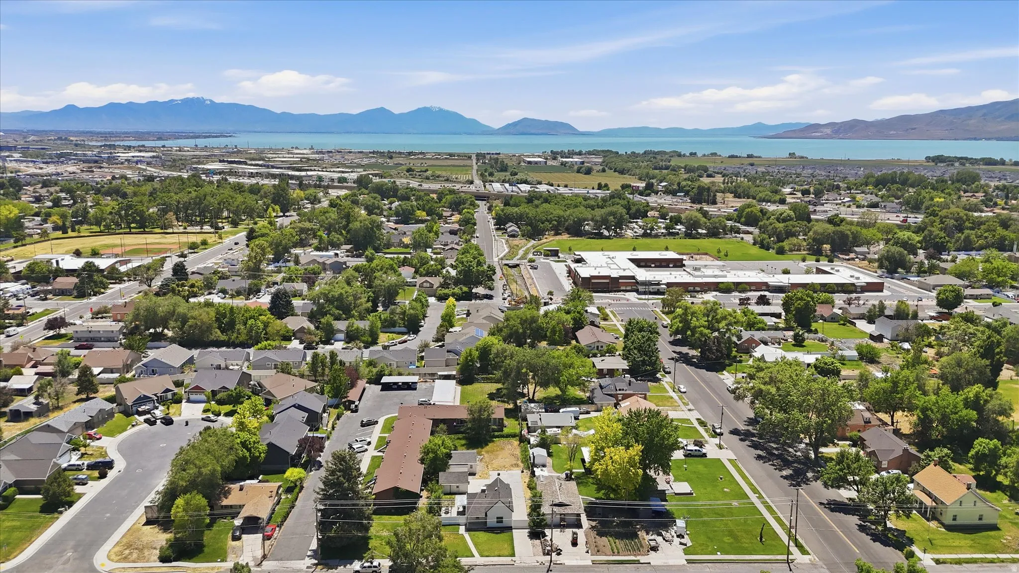 Expansive aerial perspective showcasing a residential neighborhood with verdant trees, diverse housing styles, and a prominent road system