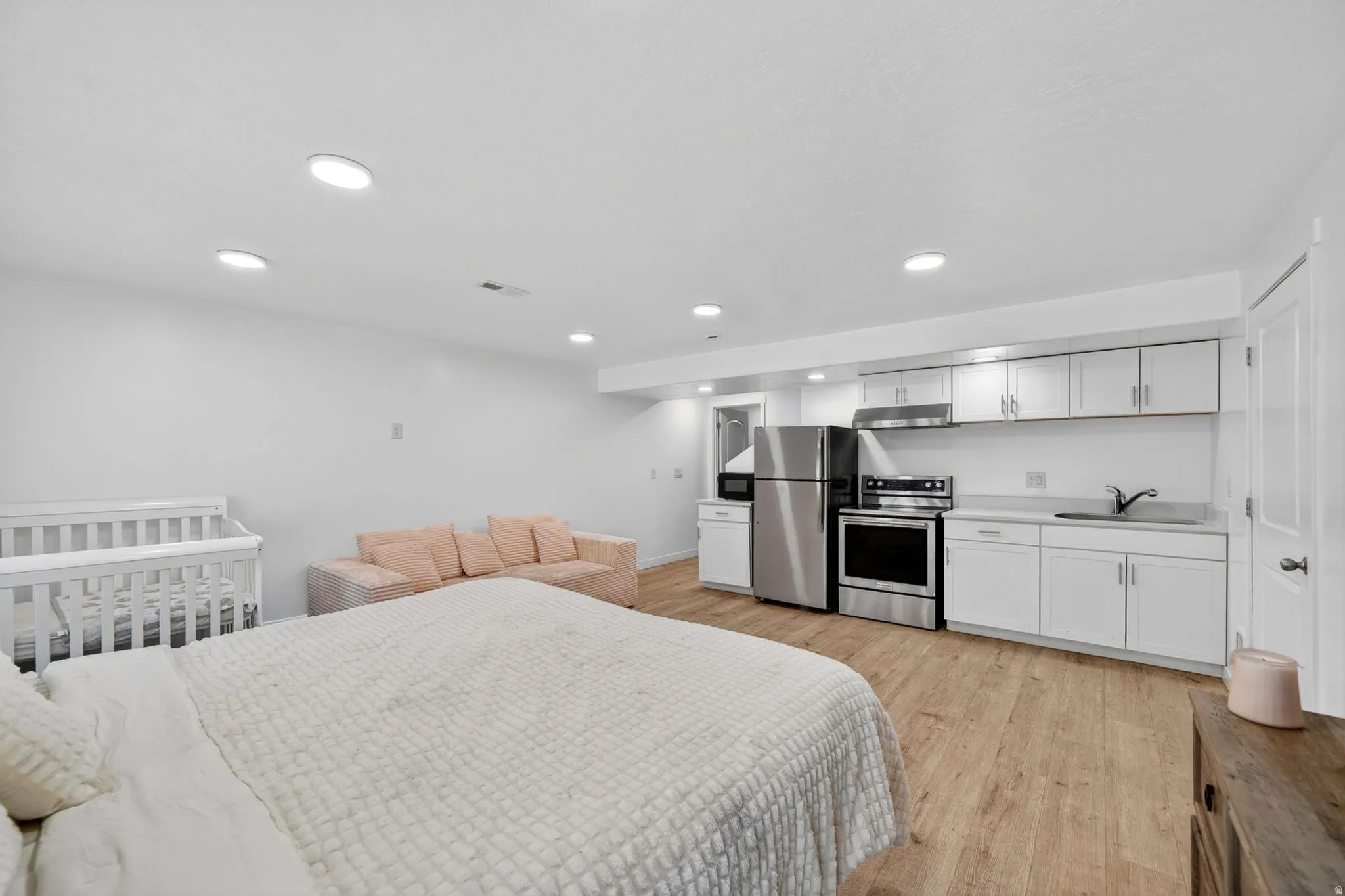 Spacious studio layout featuring a full kitchen with stainless steel appliances, ample white cabinetry, and wood-finish flooring