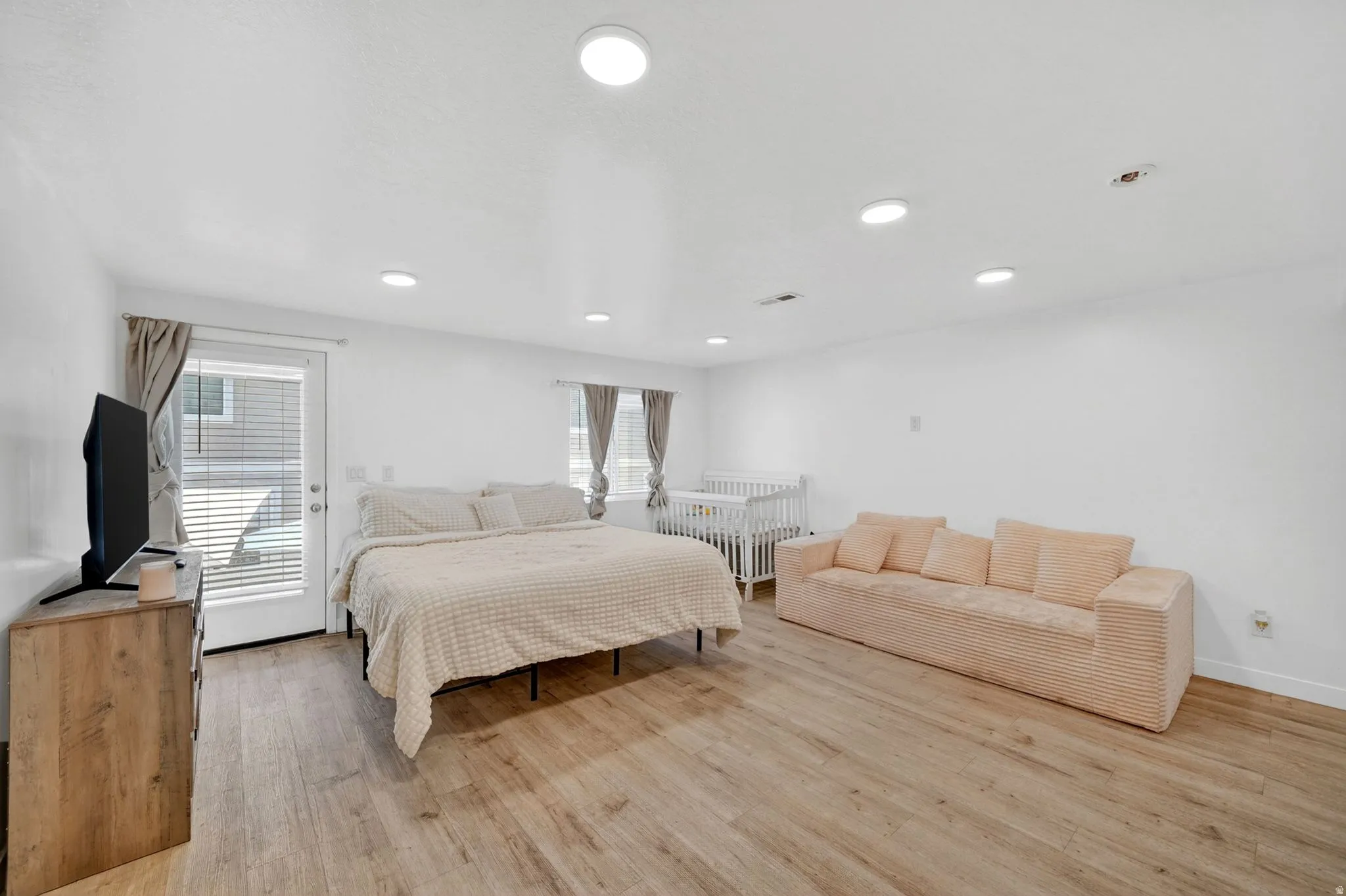 Spacious room featuring wood-finish flooring, recessed lighting, white walls, and a glass-paneled exterior door with blinds